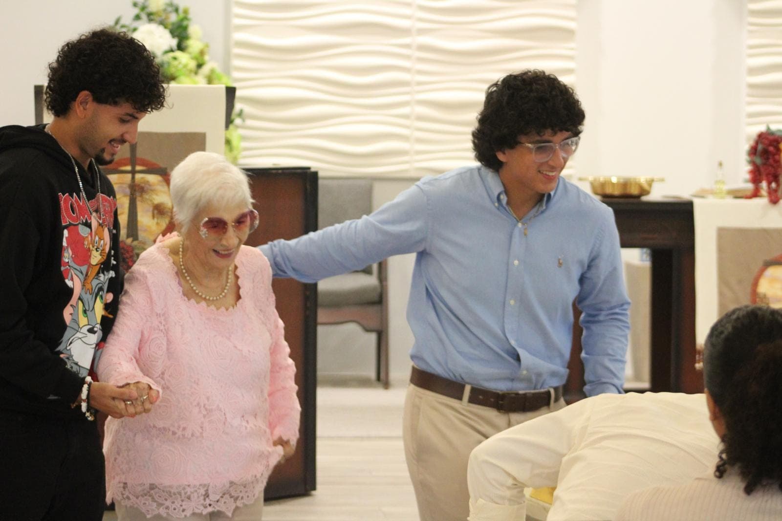Una mujer mayor camina del brazo de dos jóvenes, sonriendo.