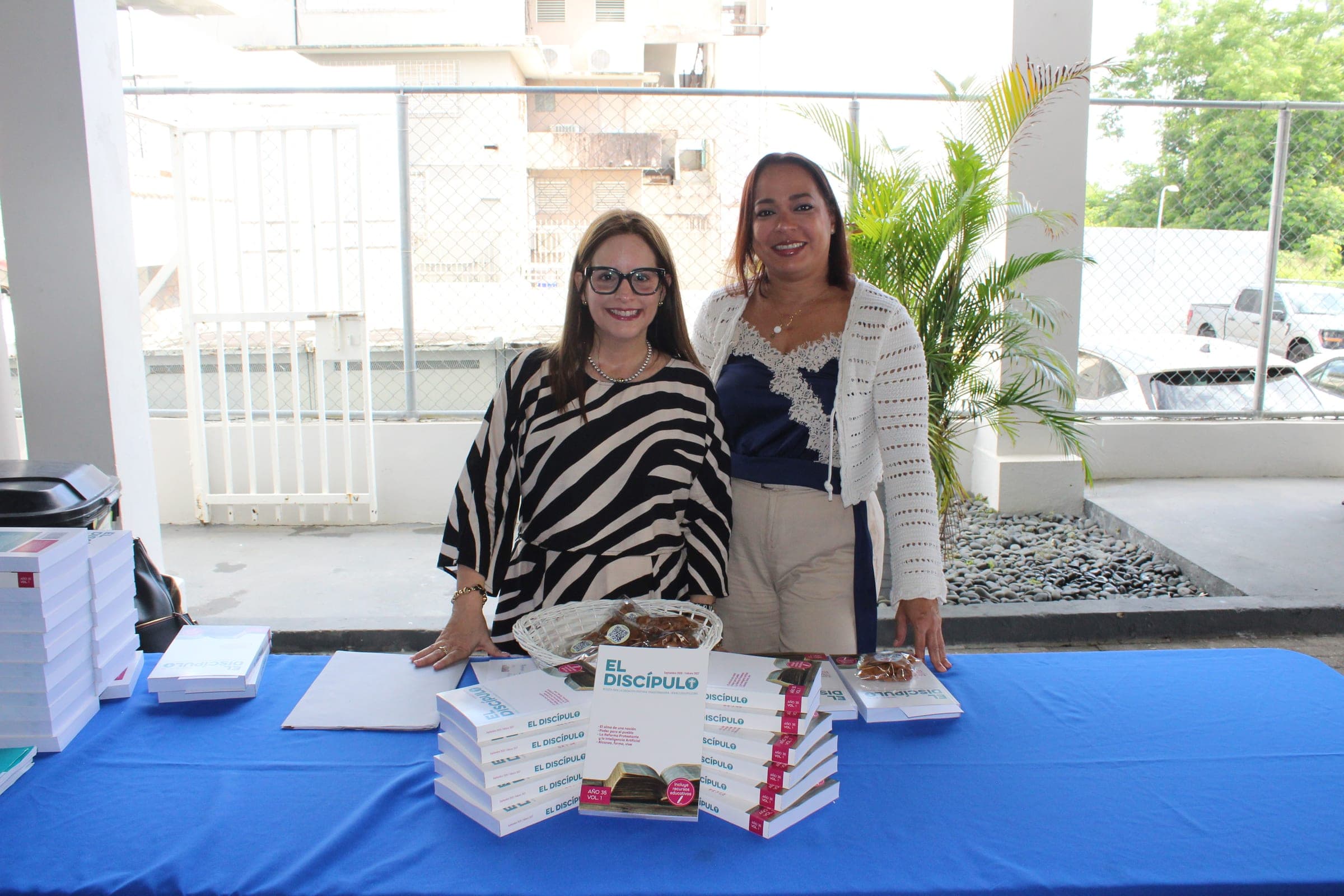 Dos mujeres sonríen junto a la mesa de bienvenida con la revista El Discípulo.